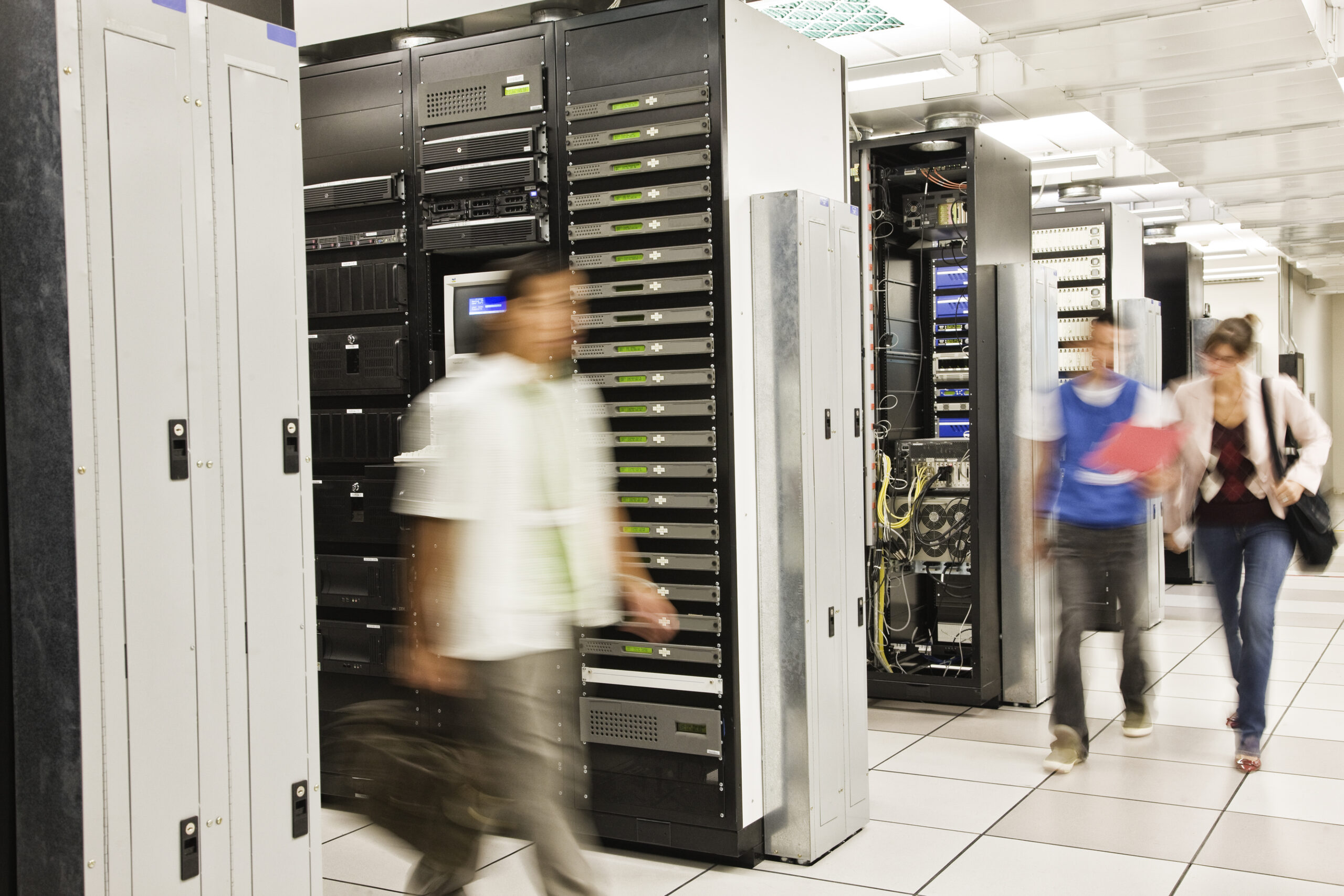 Drei Techniker in einem großen Serverraum mit mehreren Server-Racks, die an IT-Infrastruktur arbeiten, symbolisieren IT Solutions, Managed Services und Datacenter Solutions.