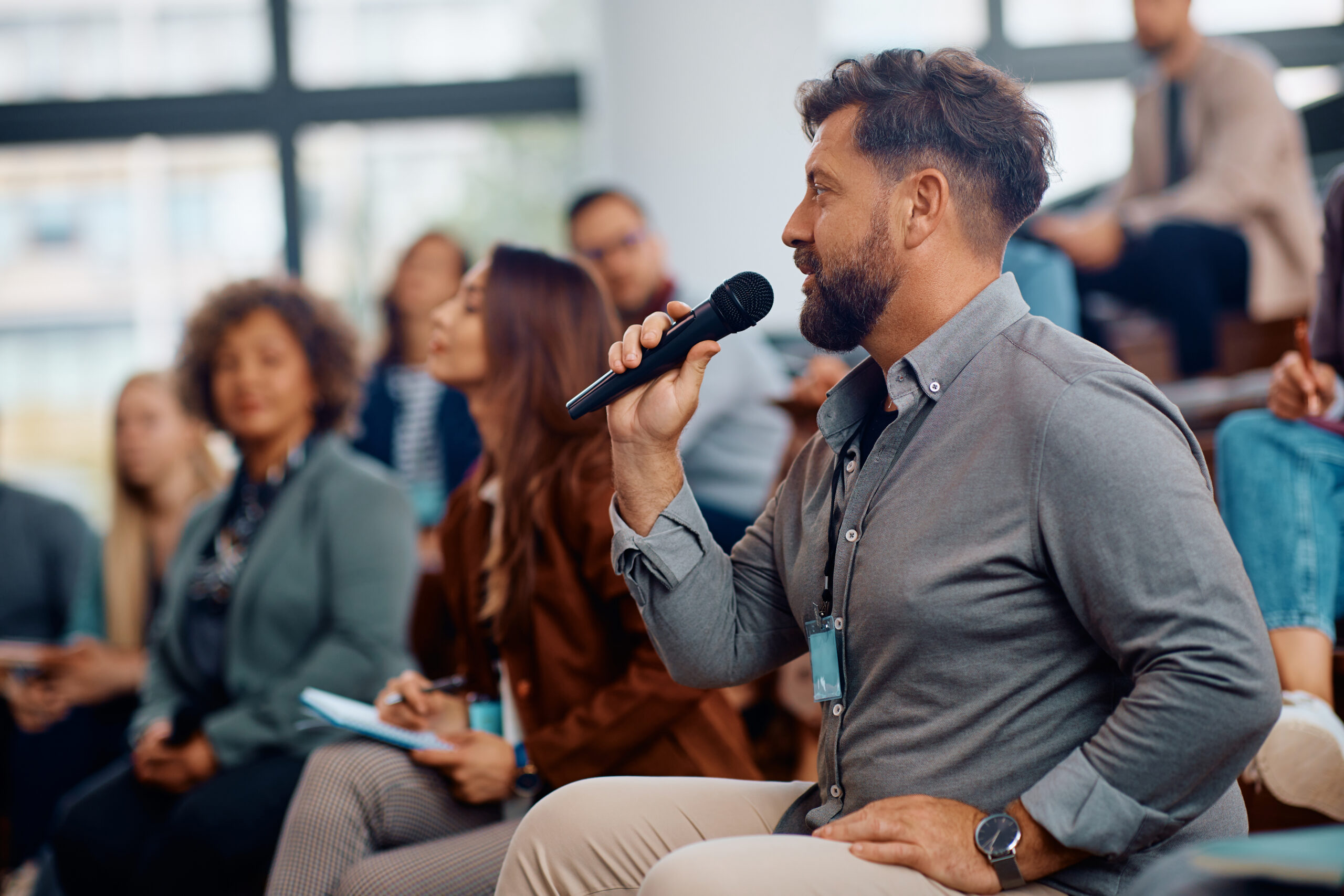 Mann mit Mikrofon stellt Frage bei Business-Seminar, umgeben von weiteren Teilnehmern in moderner Konferenzhalle, symbolisiert IT-Beratung und Kommunikationstechnik bei dierckgroup.